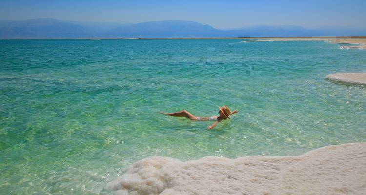 Frau schwimmt mühelos auf dem salzigen türkisfarbenen Wasser des Toten Meeres in der Nähe einer weißen Salzschicht.