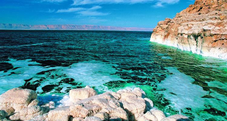 Strahlend grüne und blaue Wasser des Toten Meeres lecken an weiße salzverkrustete Klippen.