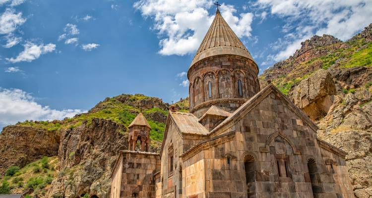 Altes Steinkloster unter blauem Himmel mit felsigem Gelände.