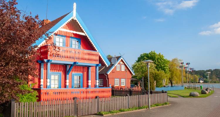 Brightly painted wooden houses with blue trim and picket fences along a lagoon under clear skies.