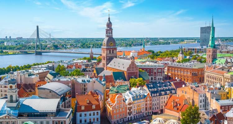 Panoramic view of Riga’s Old Town roofs with the cathedral spire, Daugava River and Vansu Bridge under a clear blue sky
