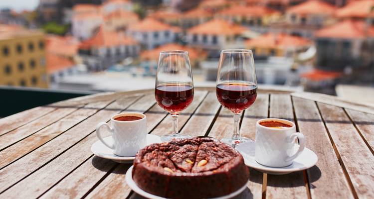 Ensemble de table en terrasse en bois avec deux verres de vin de Madère, des tasses à café et un gâteau traditionnel