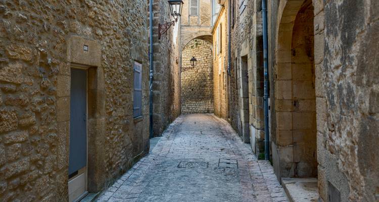 Schmale Kopfsteinpflastergasse, flankiert von verwitterten Kalksteinmauern und Fenstern mit Fensterläden.