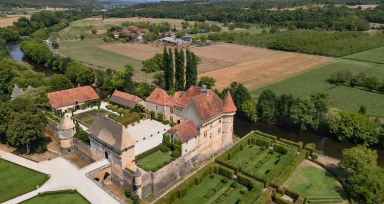 Luftaufnahme eines von einem Wassergraben umgebenen Schlosskomplexes mit gepflegten Gärten inmitten einer kleinräumig gegliederten Landschaft.
