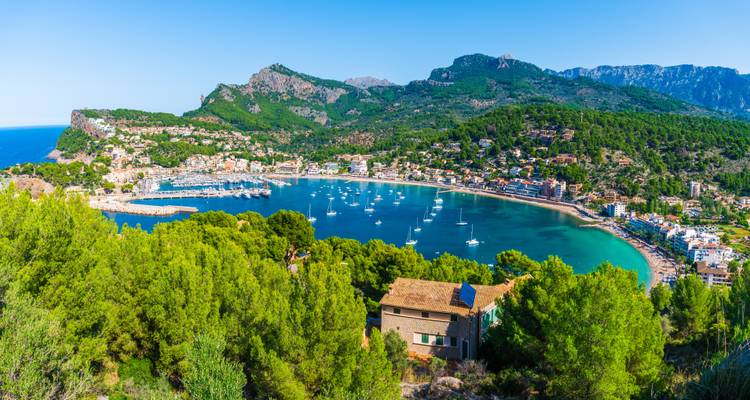 Una amplia bahía llena de veleros rodeada de colinas y montañas cubiertas de pinos en Port de Sóller.