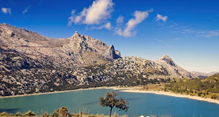 Embalse de montaña turquesa rodeado de picos de piedra caliza escarpados bajo un cielo azul brillante con nubes ligeras.