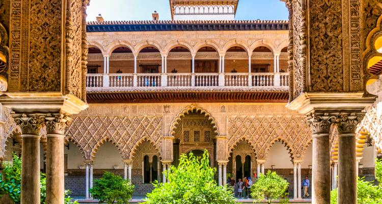 Verzierter maurischer Innenhof des Real Alcázar von Sevilla mit geschnitzten Bögen und üppigem Zentralgarten.
