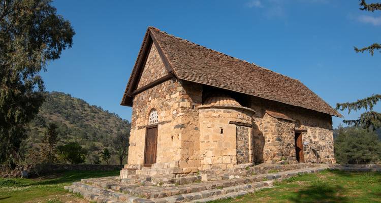 Small stone church with tiled roof stands on a grassy terrace under a clear sky