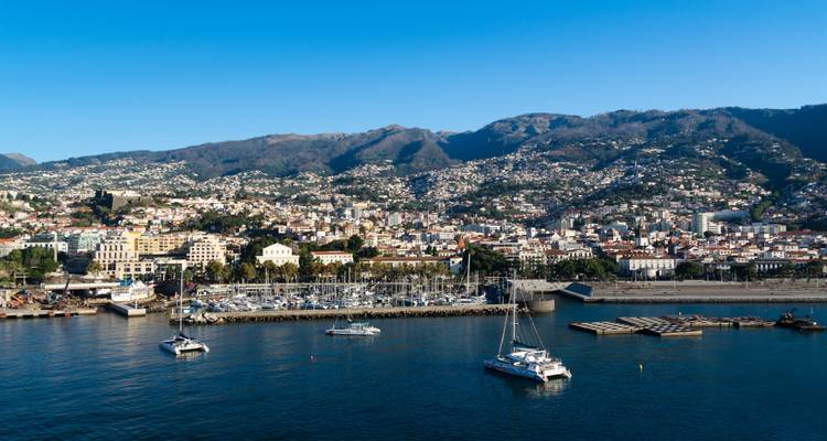 Coastal cityscape with yachts and distant hills.