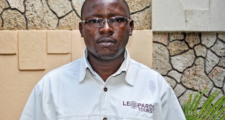 Porträt eines Mannes in einem Hemd mit Logo, der vor einer Steinmauer steht.