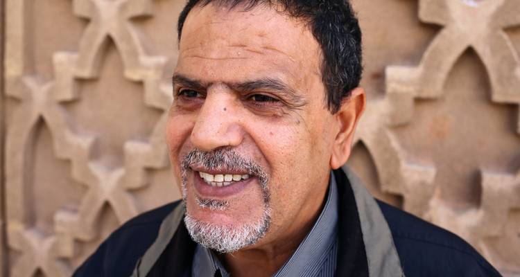 Portret van een glimlachende man tegen een gemuurde muur.