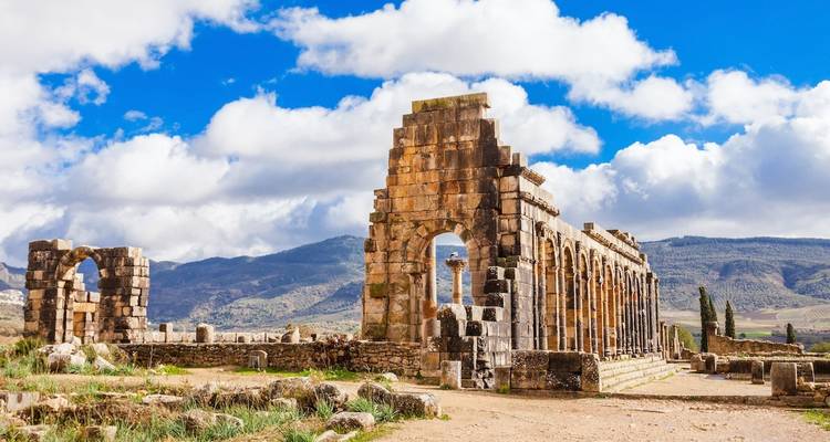 Oude ruïnes met bogen en bergen op de achtergrond.