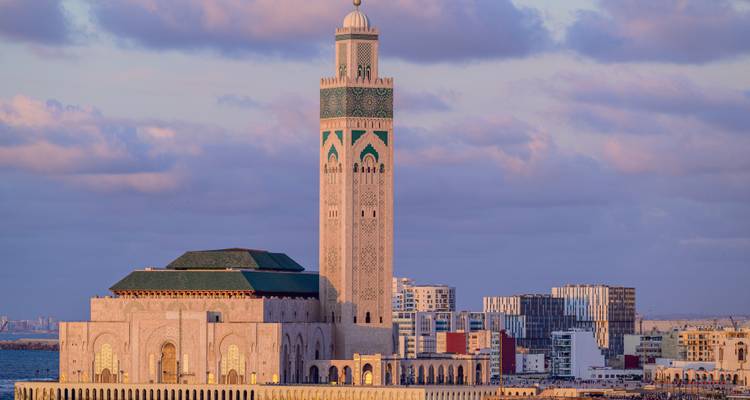 Elegant view of the Hassan II Mosque rising beside the Atlantic with pastel clouds and city skyline at dusk.