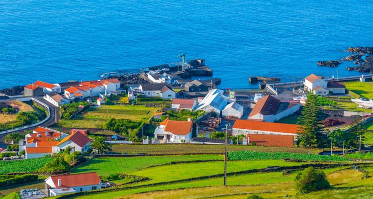 Village côtier coloré avec des maisons aux toits rouges surplombant le profond océan Atlantique bleu.