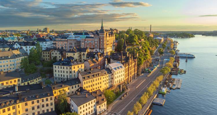 Luftaufnahme bei Sonnenaufgang über Stockholms Gamla Stan und der Uferpromenade mit goldenem Licht auf den Dächern.