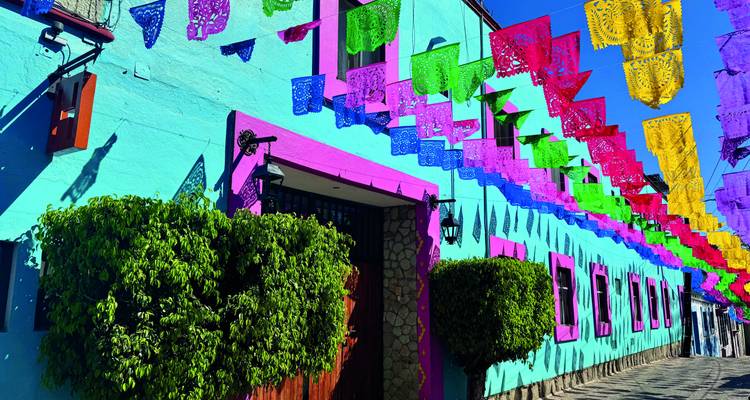 Hell leuchtend bemalte mexikanische Straße, geschmückt mit farbenfrohen Papel-Picado-Bannern vor klarem Himmel