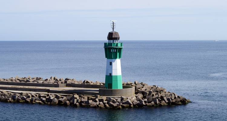 Grün-weißer Leuchtturm auf einem Wellenbrecher in ruhiger See.