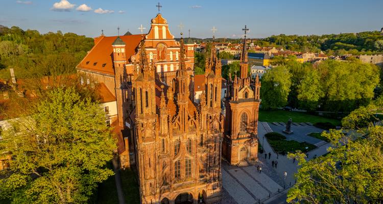 Luftaufnahme im goldenen Licht der St.-Anna-Kirche aus verziertem Backstein, umgeben von Frühlingsgrün in Vilnius.