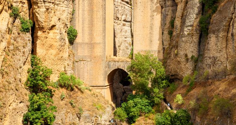 Die steilen Sandsteinklippen der Schlucht von Ronda mit hohen Brückenstützen, die in den Felsen gehauen sind.