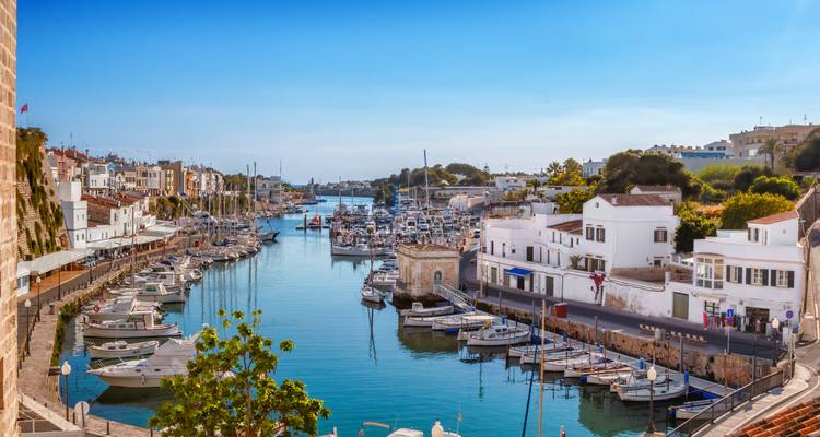 Vue panoramique du port avec des maisons blanchies à la chaux et des yachts amarrés se reflétant dans l'eau bleue calme sous un ciel dégagé.