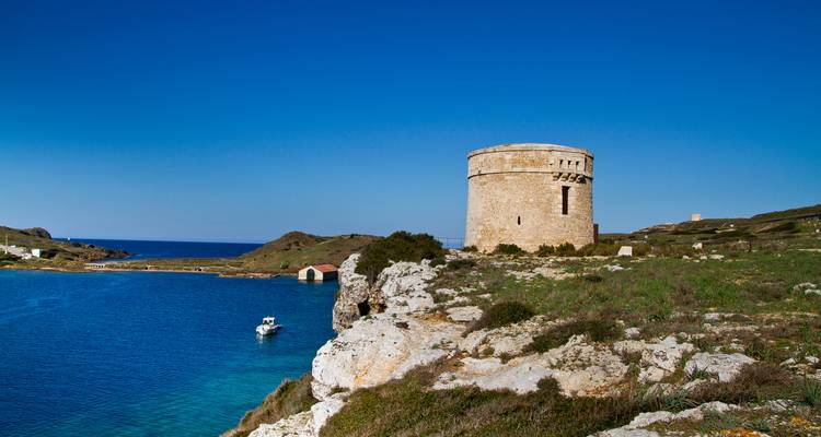 Tour de guet côtière circulaire historique dominant les eaux turquoise et le littoral accidenté sous un ciel sans nuages.