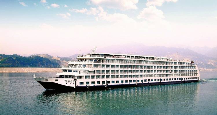 Großes weißes Kreuzfahrtschiff, das auf einem Fluss mit Bergkulisse fährt.