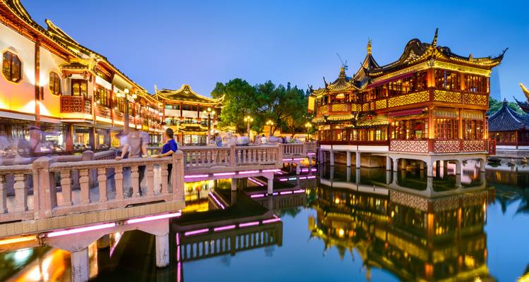 Traditionelle beleuchtete Gebäude und gewölbte Brücke spiegeln sich bei Abenddämmerung im Wasser in einem lebendigen Altstadtviertel wider