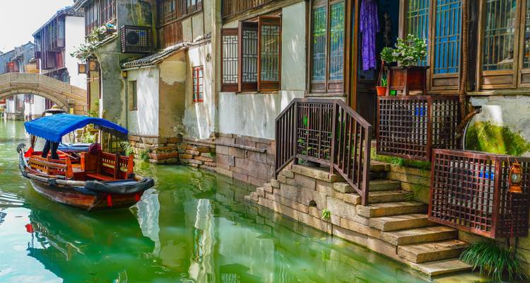 Ruhiger Kanal gesäumt von historischen weiß getünchten Häusern und einem Holzboot unter einer Steinbrücke