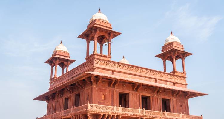 Ein roter Sandsteinpavillon mit drei Kuppeln vor blauem Himmel.
