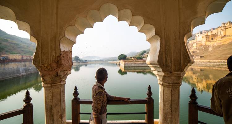 Ein Mann, der von einem verzierten Pavillon auf einen See und eine Festung blickt.