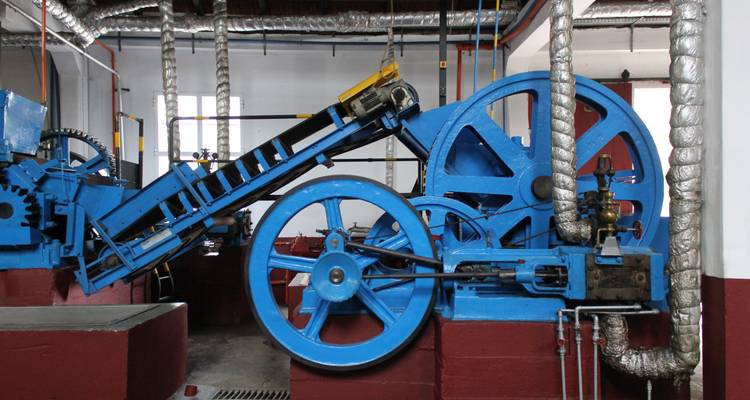 Machines bleues industrielles à l'intérieur d'une usine avec des tuyaux métalliques et des plateformes rouges.