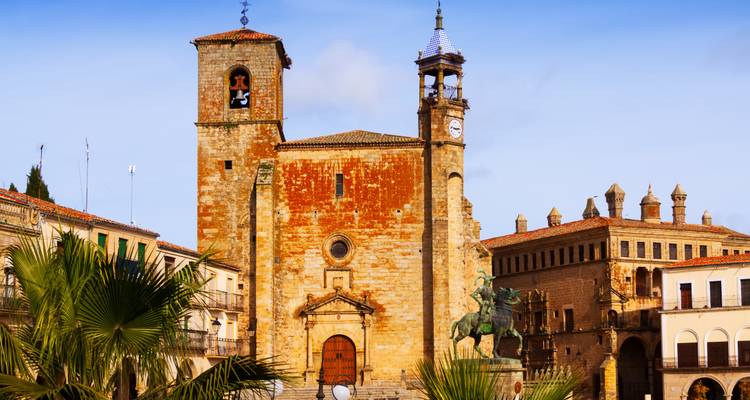 Historischer Platz in Trujillo mit Kirche aus rötlichem Stein und Reiterstatue unter klarem Himmel