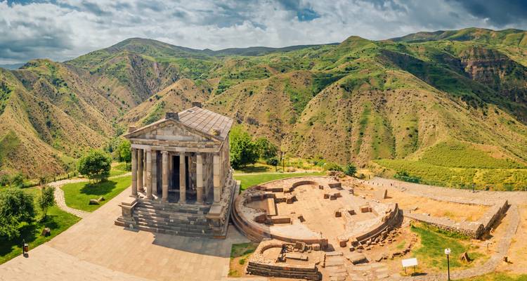 Antiker heidnischer Garni-Tempel mit Blick auf eine dramatische grüne Bergschlucht unter teilweise bewölktem Himmel.