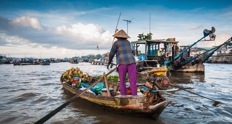 Scène de marché flottant avec une personne ramant dans un bateau rempli de produits.