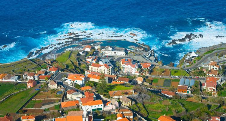 Vista aérea de un pueblo costero con piscinas naturales de lava junto a las profundas olas azules del Atlántico.
