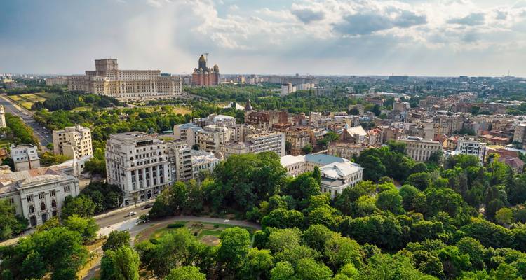Panorama aéreo de Bucarest con el Palacio del Parlamento dominando el horizonte por encima de los verdes parques de la ciudad.