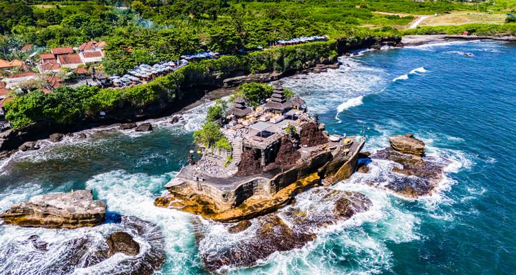 Dramatische Drohnenaufnahme des Meerestempels Tanah Lot, der auf einer felsigen Insel inmitten tosender Wellen thront.