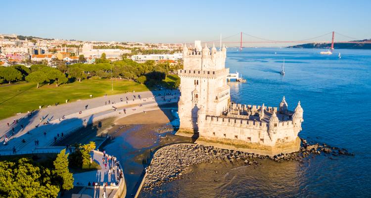 Eine Luftaufnahme bei Sonnenuntergang des Belém-Turms am Fluss Tejo mit der Brücke 25 de Abril im Hintergrund.