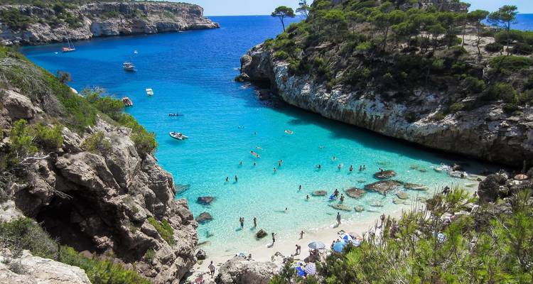 Türkisfarbenes Wasser eines Strandes mit schwimmenden Menschen, umgeben von Klippen.