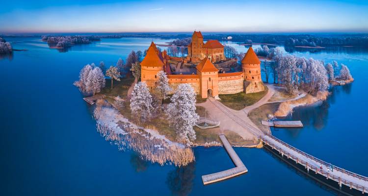 Drohnenaufnahme der Burg auf der Trakai-Insel, umgeben von gefrorenen Seen und Bruecken in der Morgenroete