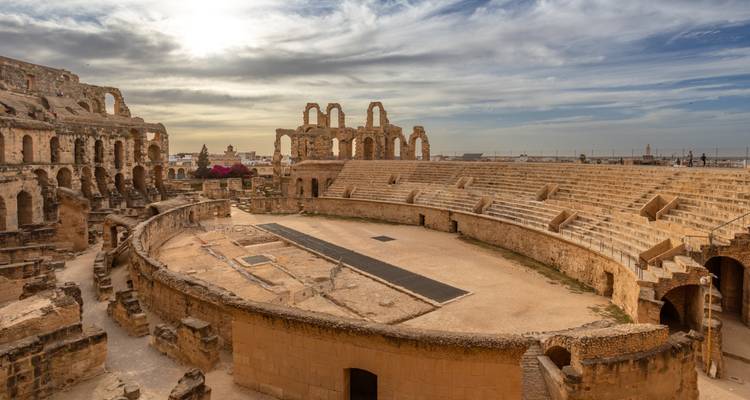 Sonnengeküsstes römisches Amphitheater mit Bögen und gestuften Steinplätzen unter einem dramatischen bewölkten Himmel im spätnachmittäglichen Licht.