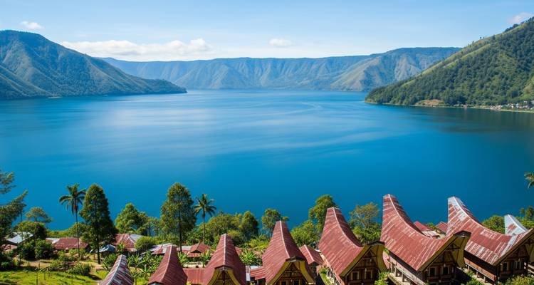 Uitgestrekt blauw Tobameer omringd door steile beboste calderawanden met traditionele Batak-daken op de voorgrond.
