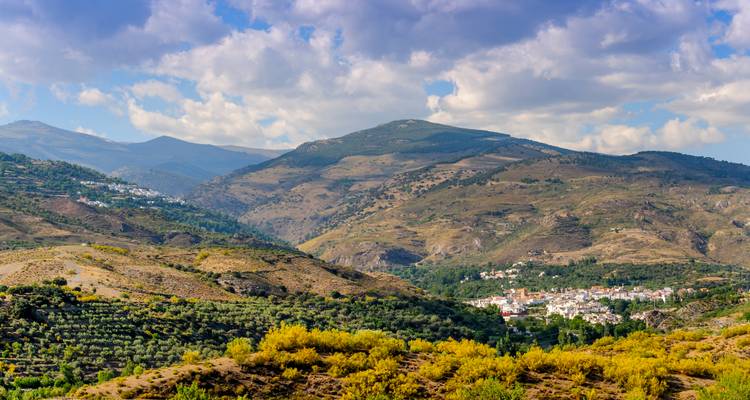 Weitläufige Bergtallandschaft der Sierra Nevada mit verstreuten weißen Dörfern und Olivenhainen.