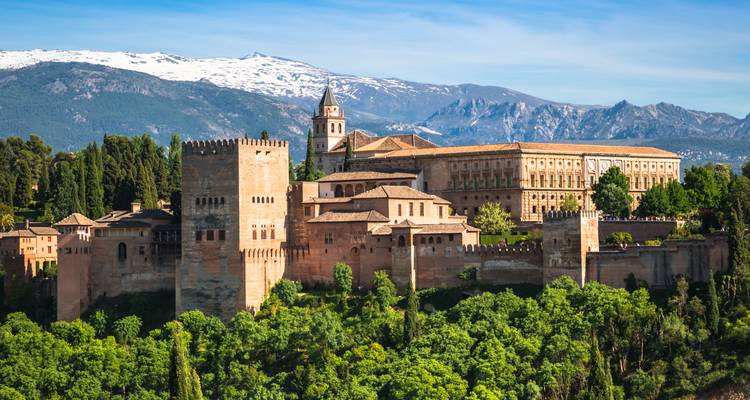 Panoramablick auf den Palastkomplex der Alhambra, umgeben von üppiger Vegetation mit den schneebedeckten Bergen der Sierra Nevada im Hintergrund