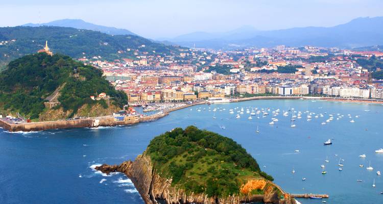 Mirador con vistas increíbles de la Bahía de La Concha en San Sebastián, llena de veleros y una isla verde y frondosa bajo la luz del día.