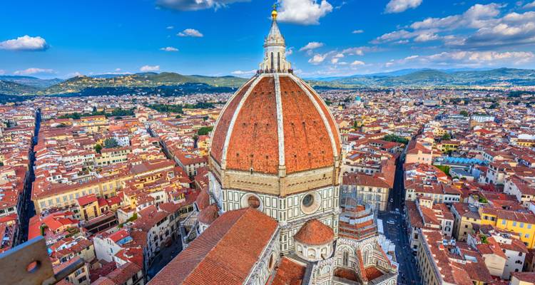 Spektakuläre Luftaufnahme von Florenz mit der ikonischen rotgeziegelten Domkuppel, die sich über ein Meer von Terrakotta-Dächern vor einem bergigen Horizont erhebt.