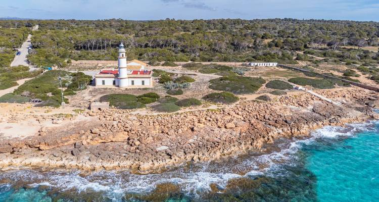 White lighthouse on a rocky coastline surrounded by turquoise water