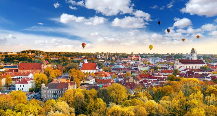 Herbstliche Luftaufnahme der Altstadt von Vilnius mit farbenfrohen Bäumen und Heißluftballons, die in einem leuchtend blauen Himmel schweben.