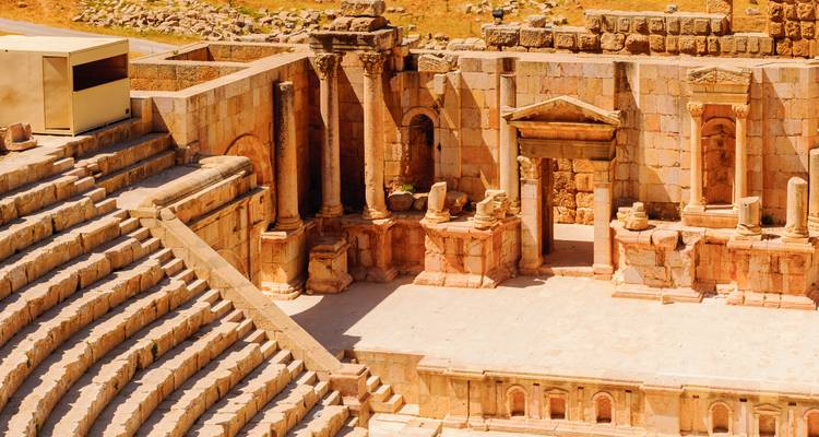 Ruinen eines antiken römischen Steintheaters mit stufenförmigen Sitzreihen und verzierter Bühnenwand.