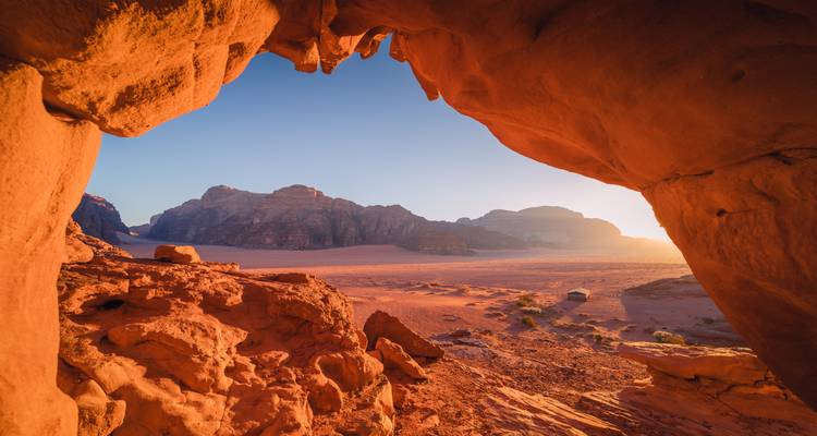Wüstenlandschaft von Wadi Rum, betrachtet aus dem Inneren eines Sandsteinbogens bei Sonnenaufgang.